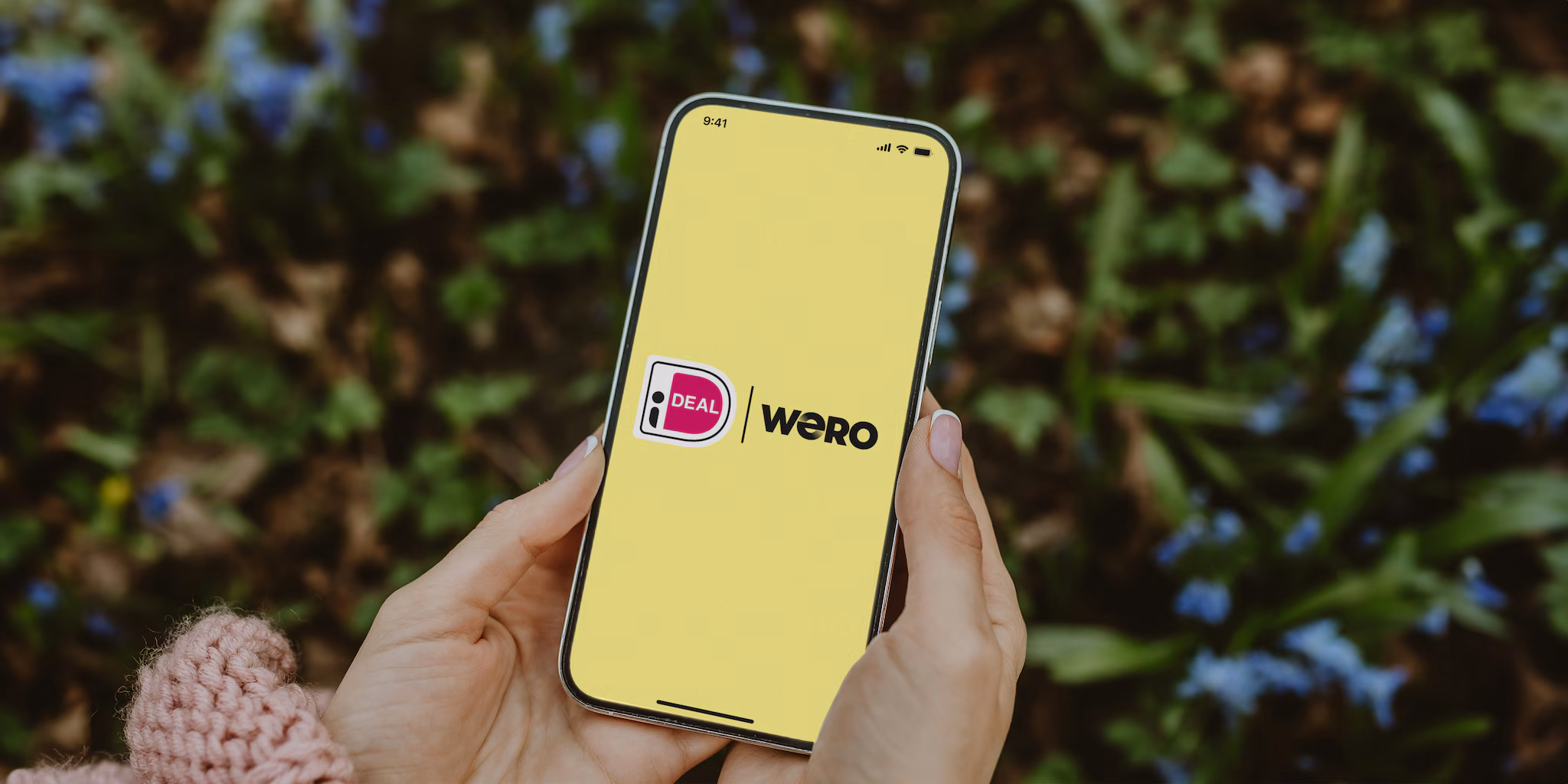 Vrouw met telefoon waarbij het ideal en WERO logo te zien is bij de struiken.
